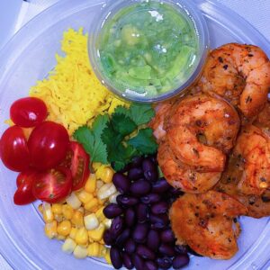 Cajun shrimp served with turmeric rice, cherry tomatoes, beans, corn, and a side of guacamole