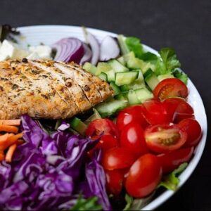 Fitaxx House Salad, made with spring mix, cucumbers, cherry tomatoes, purple cabbage, and shredded carrots. Served with a drizzle of feta cheese and balsamic vinaigrette dressing